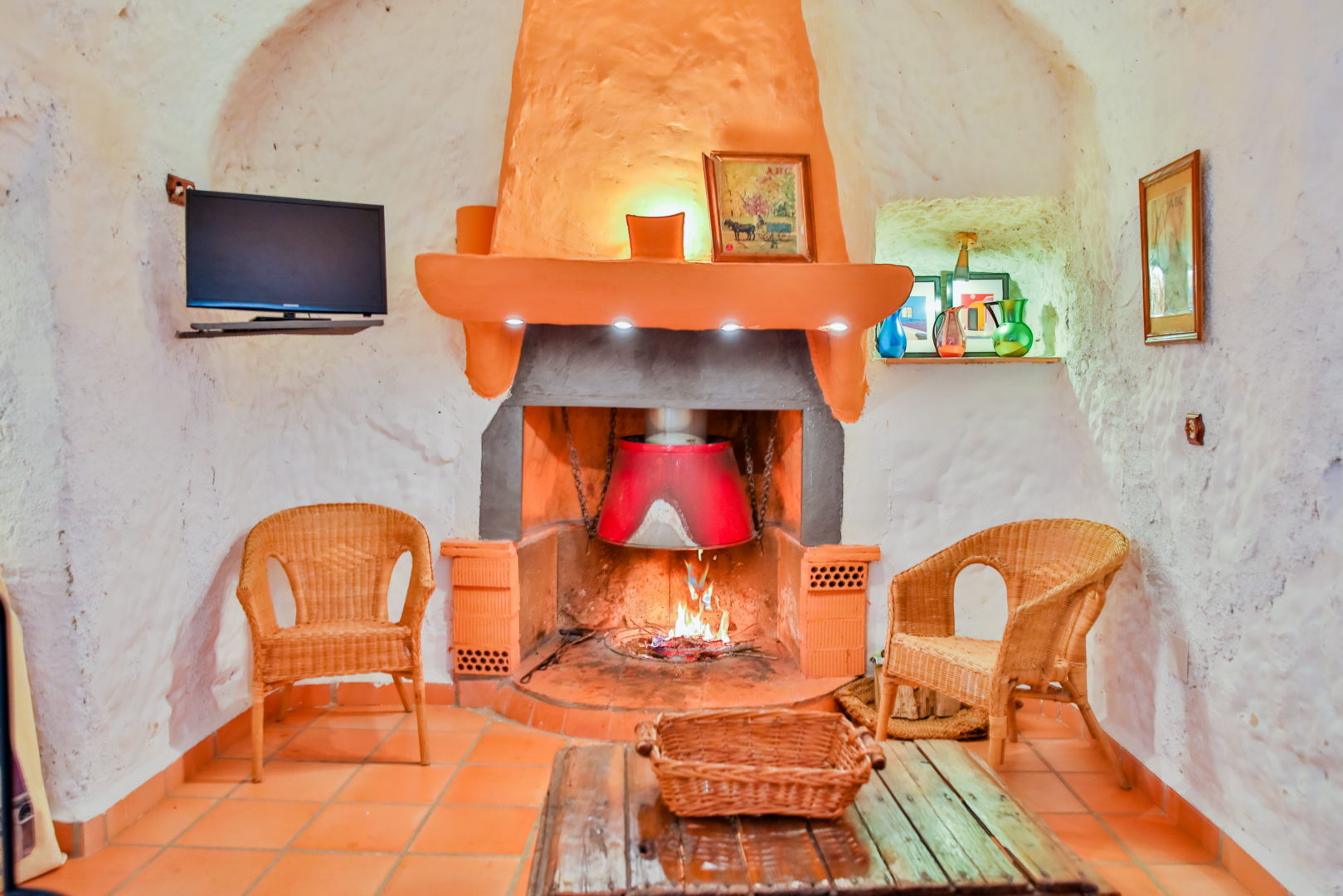 Salón de casa cueva con chimenea encendida y cerámica andaluza