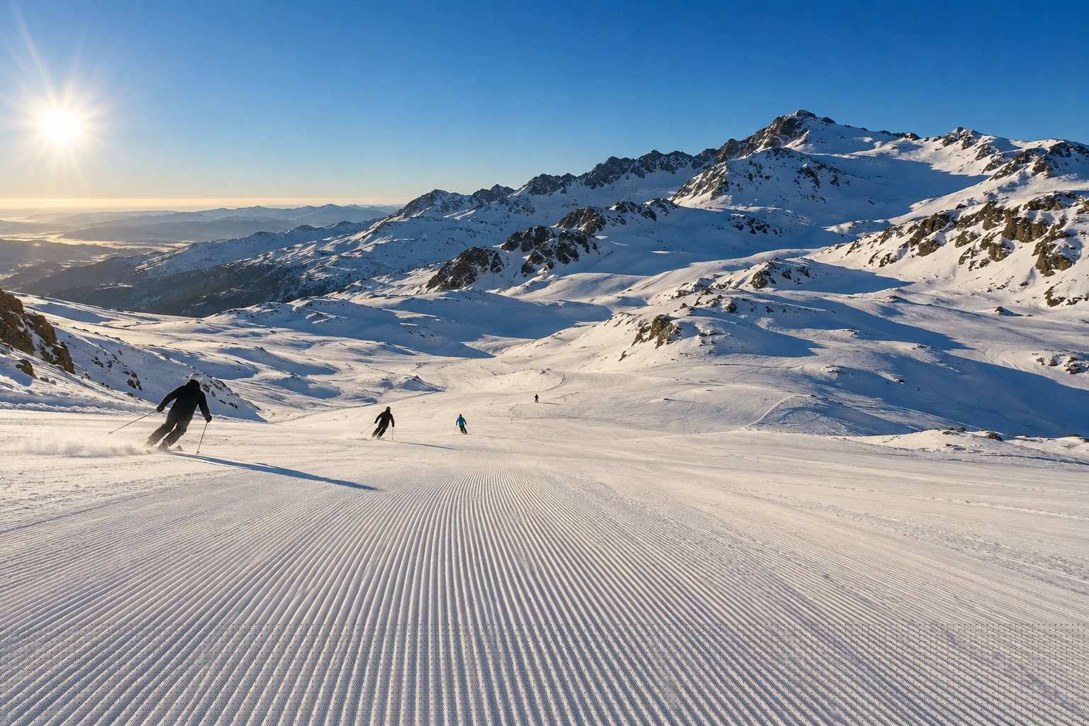 Pista de esquí recién pisada en Sierra Nevada a primera hora, con esquiadores lejanos de espaldas y el cielo azul de invierno